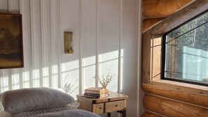 A bedroom with a large bed, a nightstand, a window, and wooden walls.