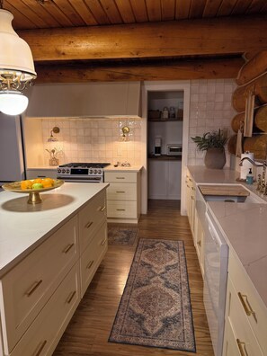 Una cocina con armarios blancos, techo de madera, estufa y pileta.