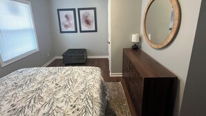 A bedroom with a bed, a dresser, a mirror, and two framed artworks on the wall.