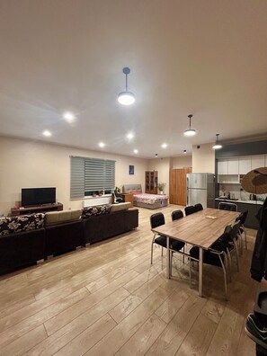 A modern living room with a sofa, TV, dining table, and chairs.