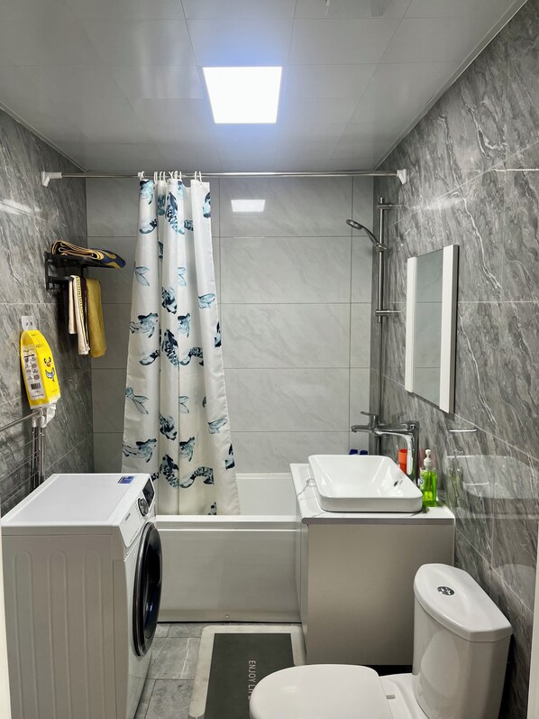 A modern bathroom with a built-in washing machine, a bathtub, a toilet, and a sink.