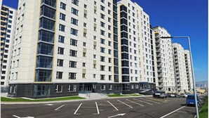 Un edificio residencial de varios pisos con un diseño moderno, que cuenta con un estacionamiento al frente.
