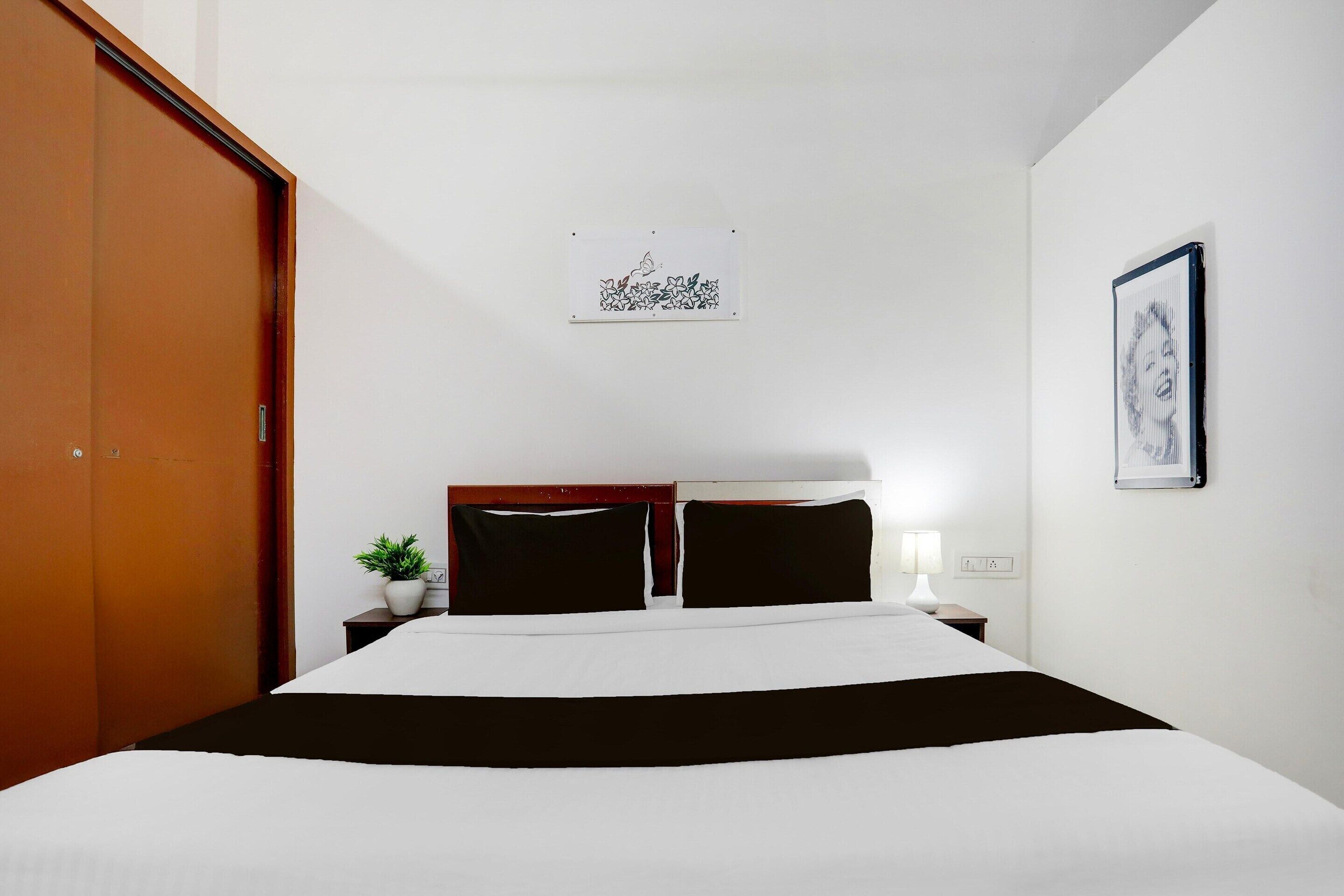 A hotel room with a bed, a nightstand, a lamp, a framed picture, and a door.