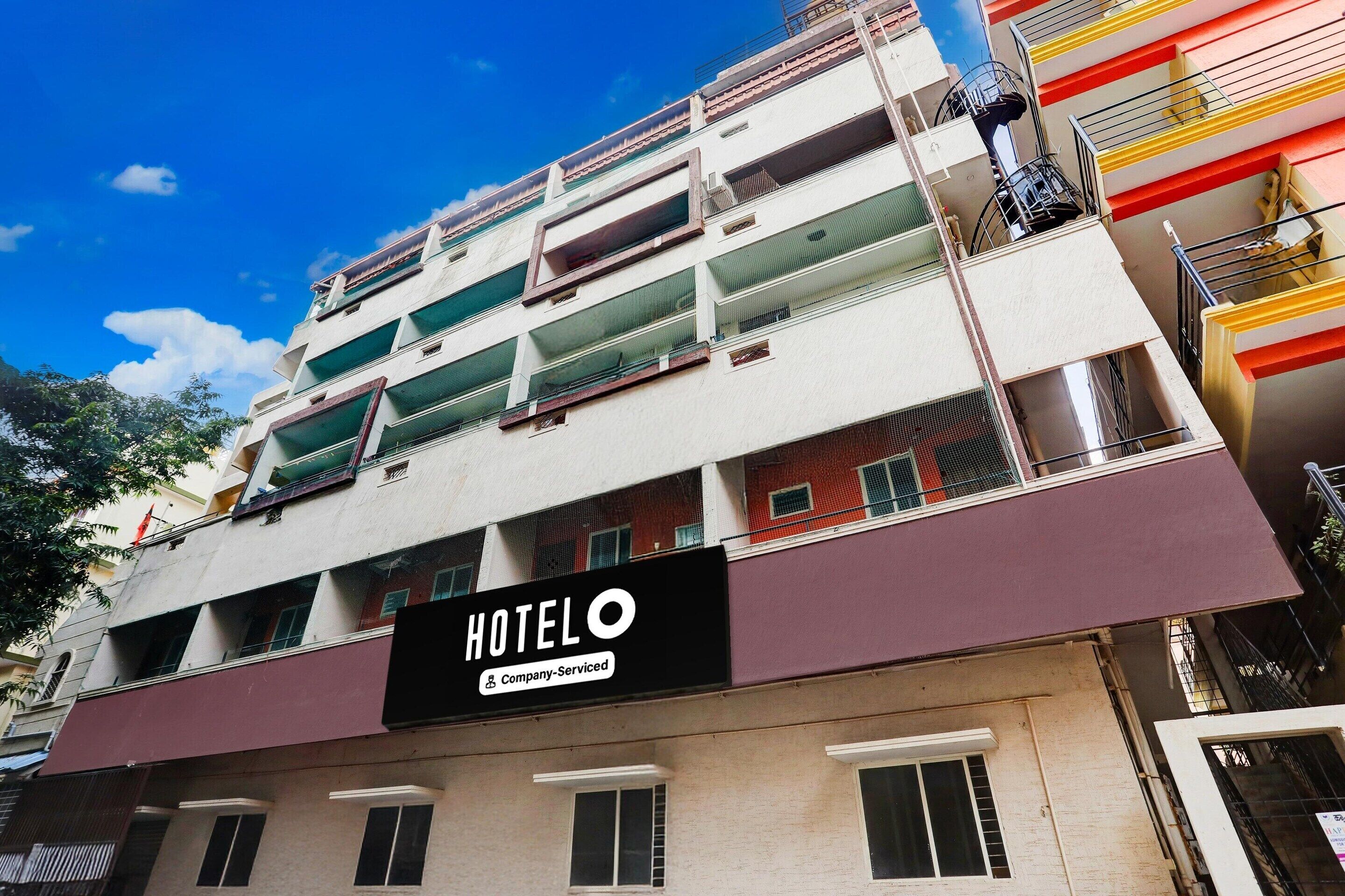 Un hôtel à plusieurs étages doté de balcons, une enseigne indiquant qu’il est géré par une entreprise, et un ciel d’un bleu limpide.