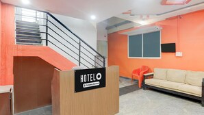 A hotel reception area with a wooden desk, a staircase, a sofa, and a window. - Deluxe Sri Krishna Nilaya (Bengaluru)