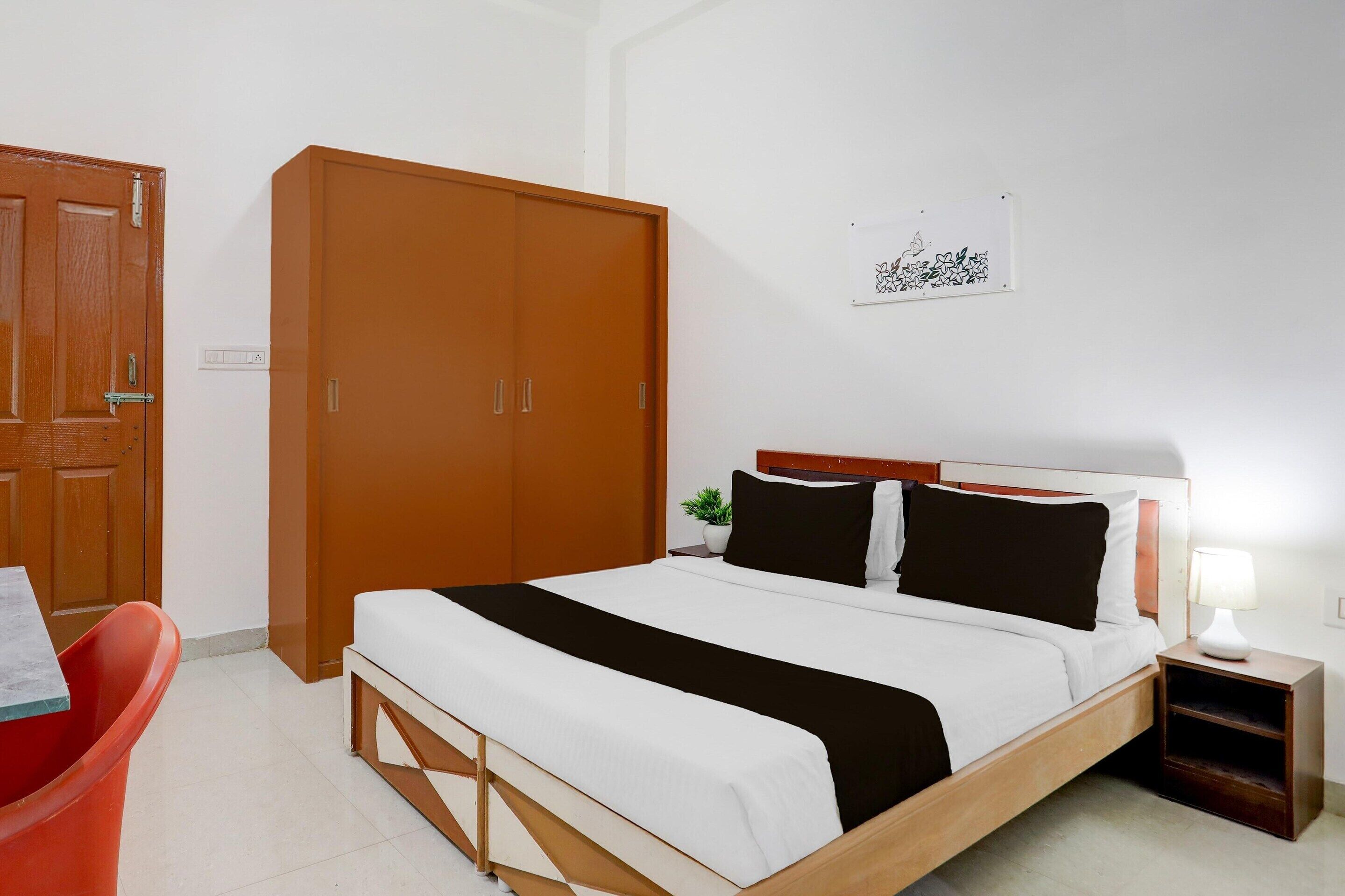 A hotel room with a bed, a wardrobe, a nightstand, a lamp, and a wall decoration.