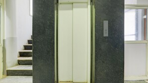 An elevator with a white interior, flanked by dark marble walls and a staircase with white steps. - Deluxe Sri Krishna Nilaya (Bengaluru)
