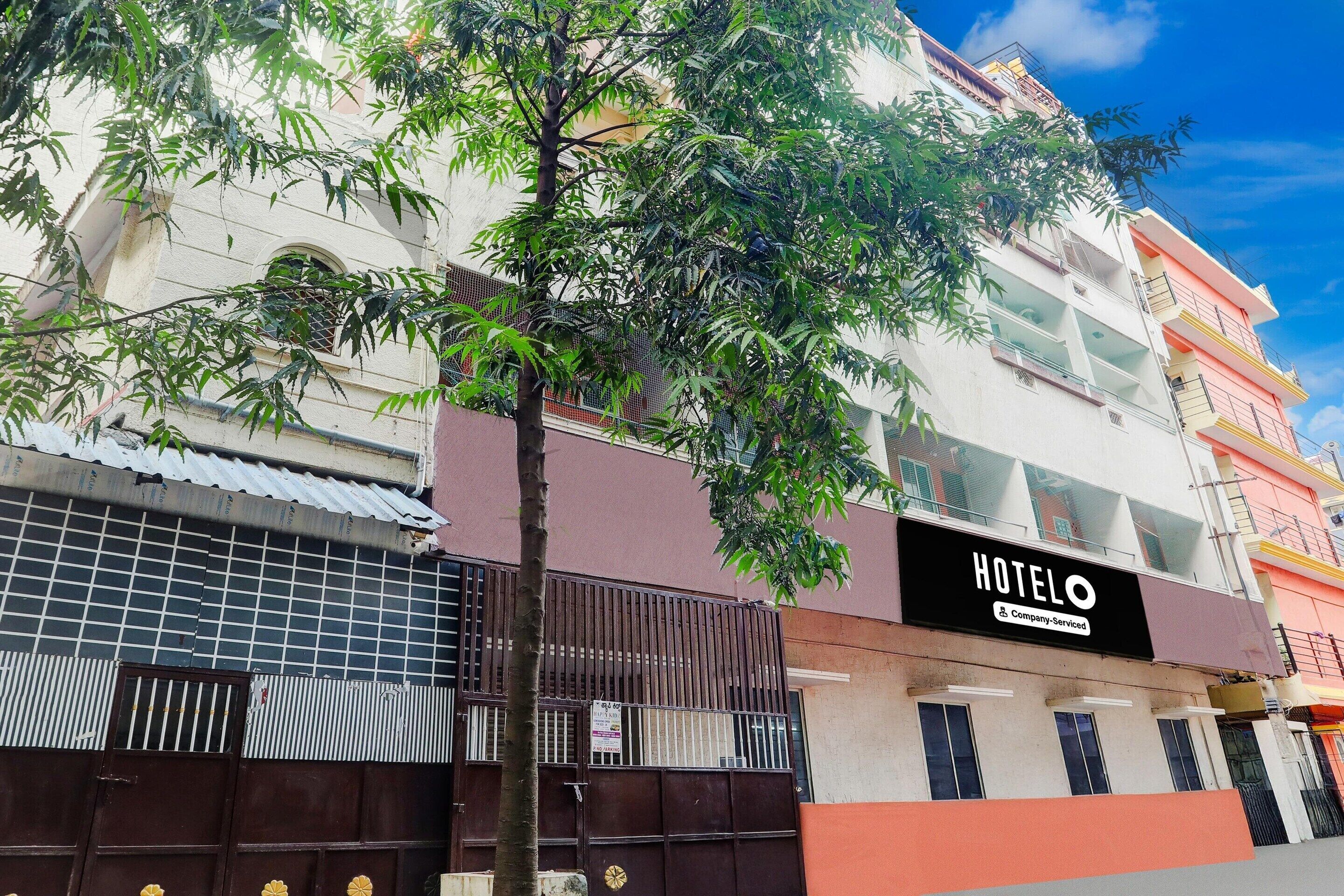 A hotel with a signboard, a gated entrance, and a tree in front.