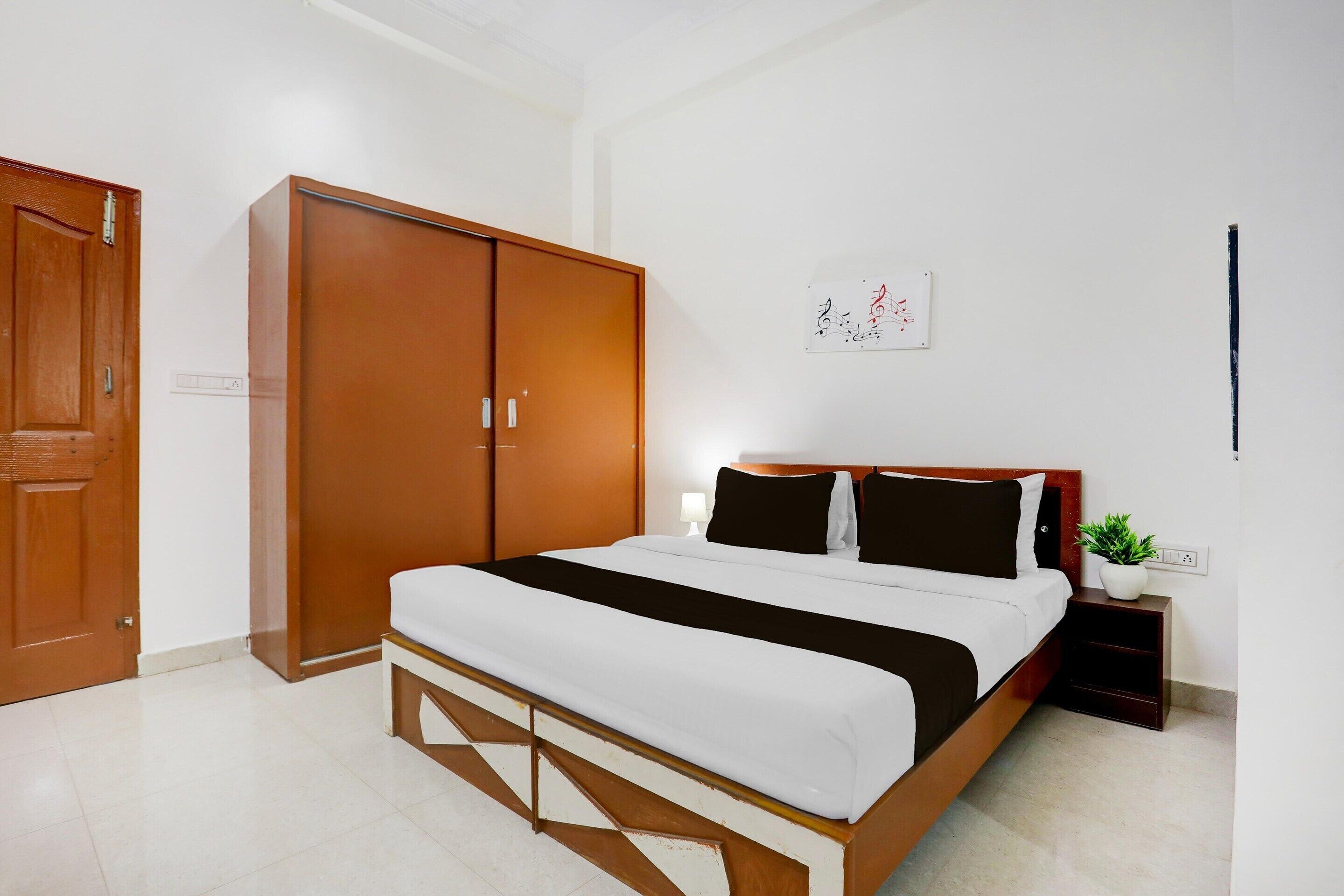 A bedroom with a bed, a wardrobe, a nightstand with a plant, and a wall-mounted artwork.
