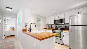 Una cocina moderna con una isla central, electrodomésticos de acero inoxidable y vistas al dormitorio contiguo.