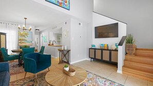 Una sala de estar moderna con sillas color turquesa, una mesa de centro, un televisor y una escalera.