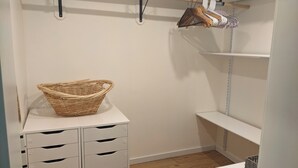 Ein Schrank mit einem Korbwannenkorb auf einer weißen Kommode, einer Kleiderstange aus Holz und einem weißen Regal.
