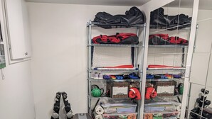Ein Fitnessraum mit einer Langhantelbank, einem großen Trainingsball und ordentlich bestellten Regalen mit diversen Gegenständen.