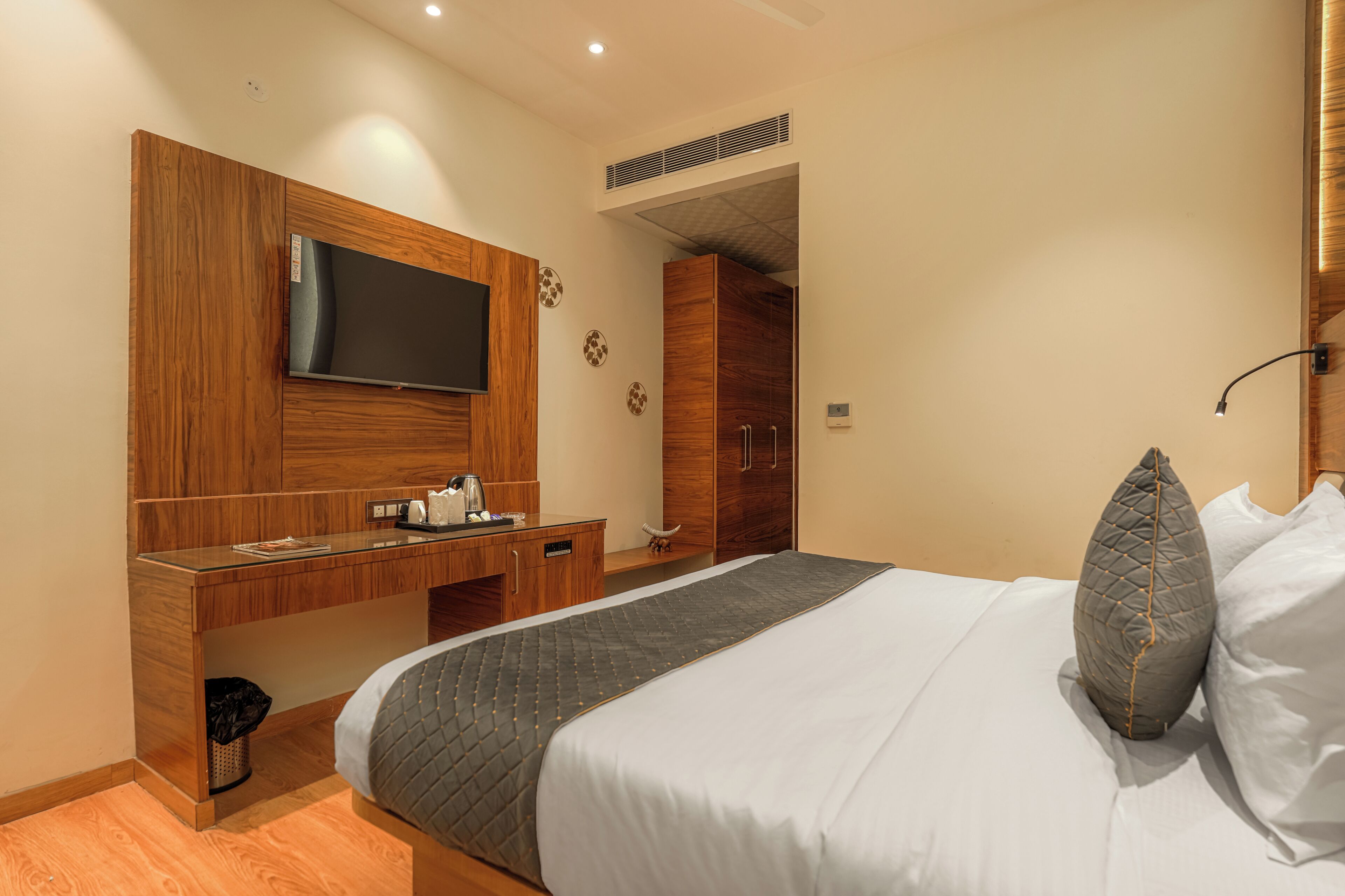 Une chambre d’hôtel comprenant un lit, un téléviseur fixé sur un panneau en bois, un bureau avec une machine à café et une armoire.