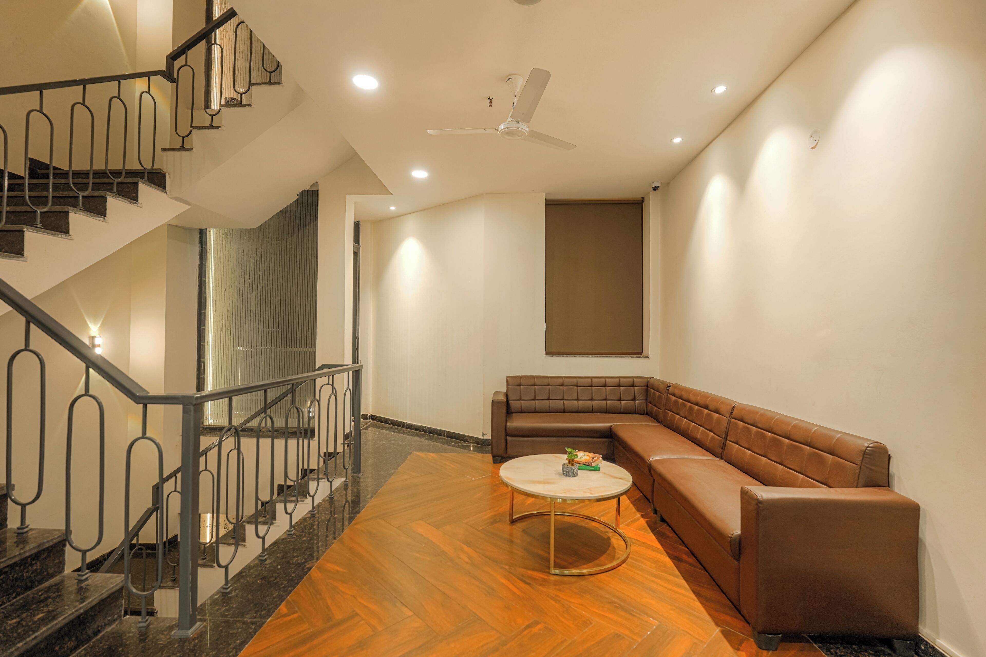 Un espacio de estar moderno con una escalera, un sofá de cuero marrón, una mesa de centro redonda y un ventilador de techo.