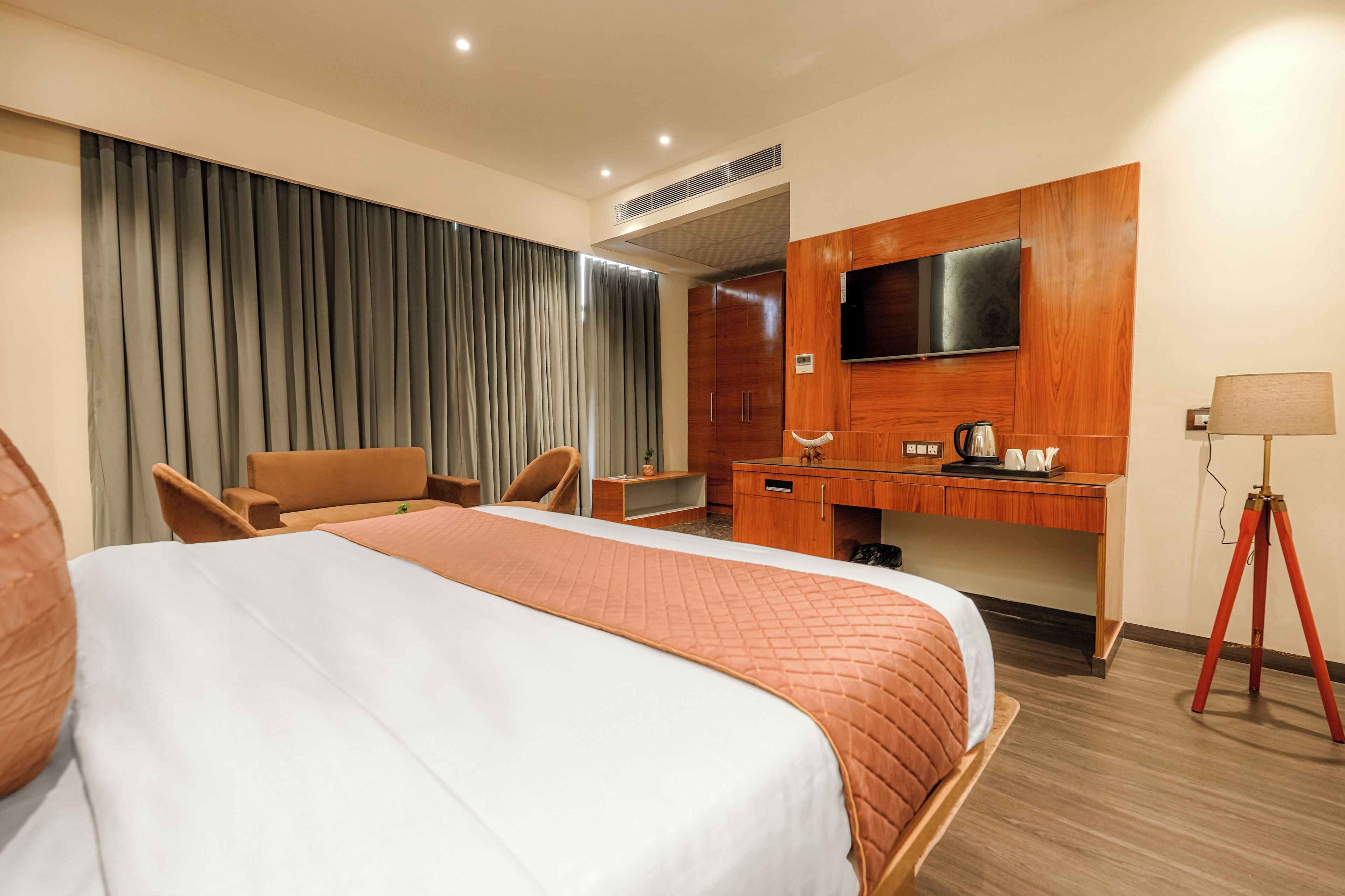 Una habitación de hotel con cama, escritorio, silla, televisor y lámpara.