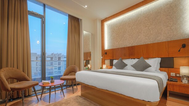 Habitación de hotel con una cama grande, dos sillones, una mesita y vistas a la ciudad.