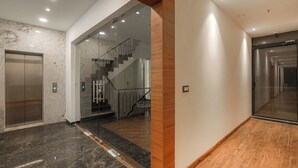 Un interior moderno con pared de mármol, suelo de madera, un ascensor de vidrio y una escalera.