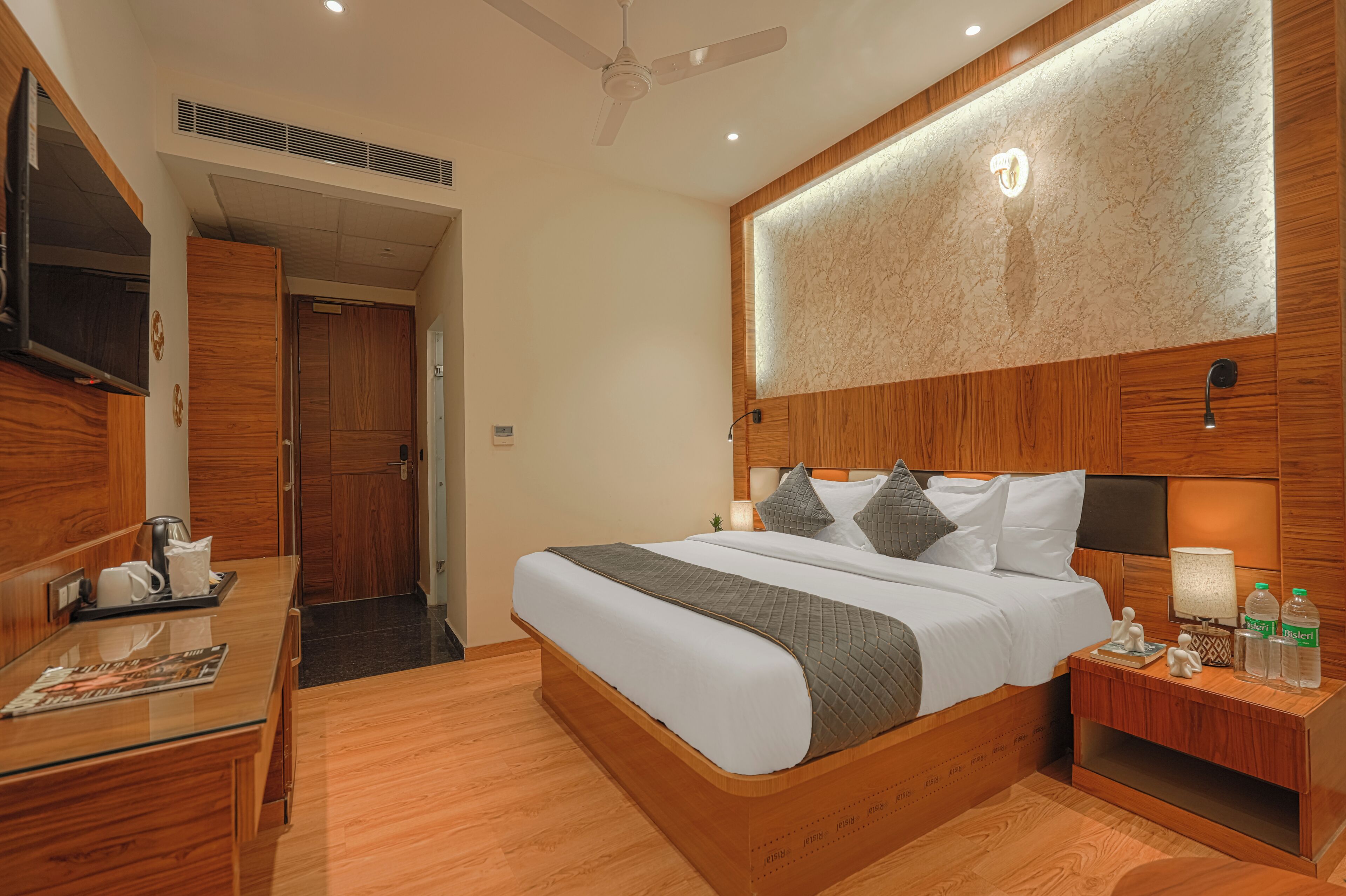 A hotel room with a bed, bedside table, and a television on the wall.