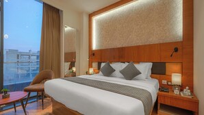 Una habitación de hotel moderna con una cama grande, cabecera de madera, lámparas de noche, mesitas de noche y vistas a la ciudad.