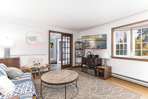 A living room with a round coffee table, a sofa, a chair, a fireplace, a bookshelf, and a window with a view of trees. - Exceptional location with both Weekapaug Beaches and Quonnie Salt Pond Access (Charlestown)