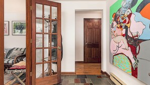 A hallway with a wooden door, a couch, and a colorful abstract painting on the wall. - Exceptional location with both Weekapaug Beaches and Quonnie Salt Pond Access (Charlestown)