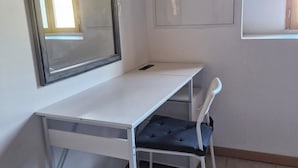 Un bureau blanc avec une chaise, un miroir et un tableau blanc dans une pièce dont le sol est recouvert de carreaux.