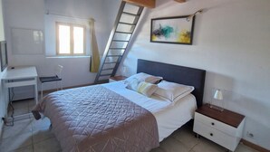 Une chambre à coucher comprenant un lit, un bureau, une chaise, une table de chevet, une lampe, une fenêtre, un tableau et un plafond en bois.