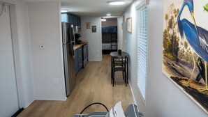 A compact kitchen with a refrigerator, microwave, and wooden cabinets. There is a bunk bed in the background and a dining area with a table and chairs. - Amelia's Hidden Hideaway/ quiet cottage located in Broussard, La. (Broussard)