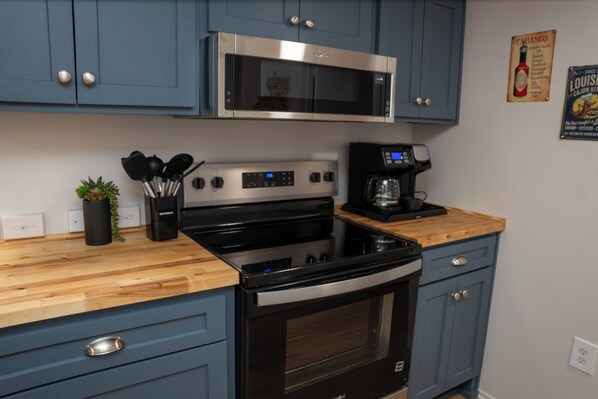 A kitchen with a microwave, stove, coffee maker, and blue cabinets.