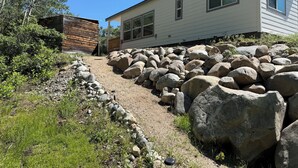 A house with a gravel driveway, large rocks, and a wooden structure.
