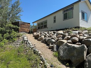 A house with a gravel driveway, large rocks, and a wooden structure.