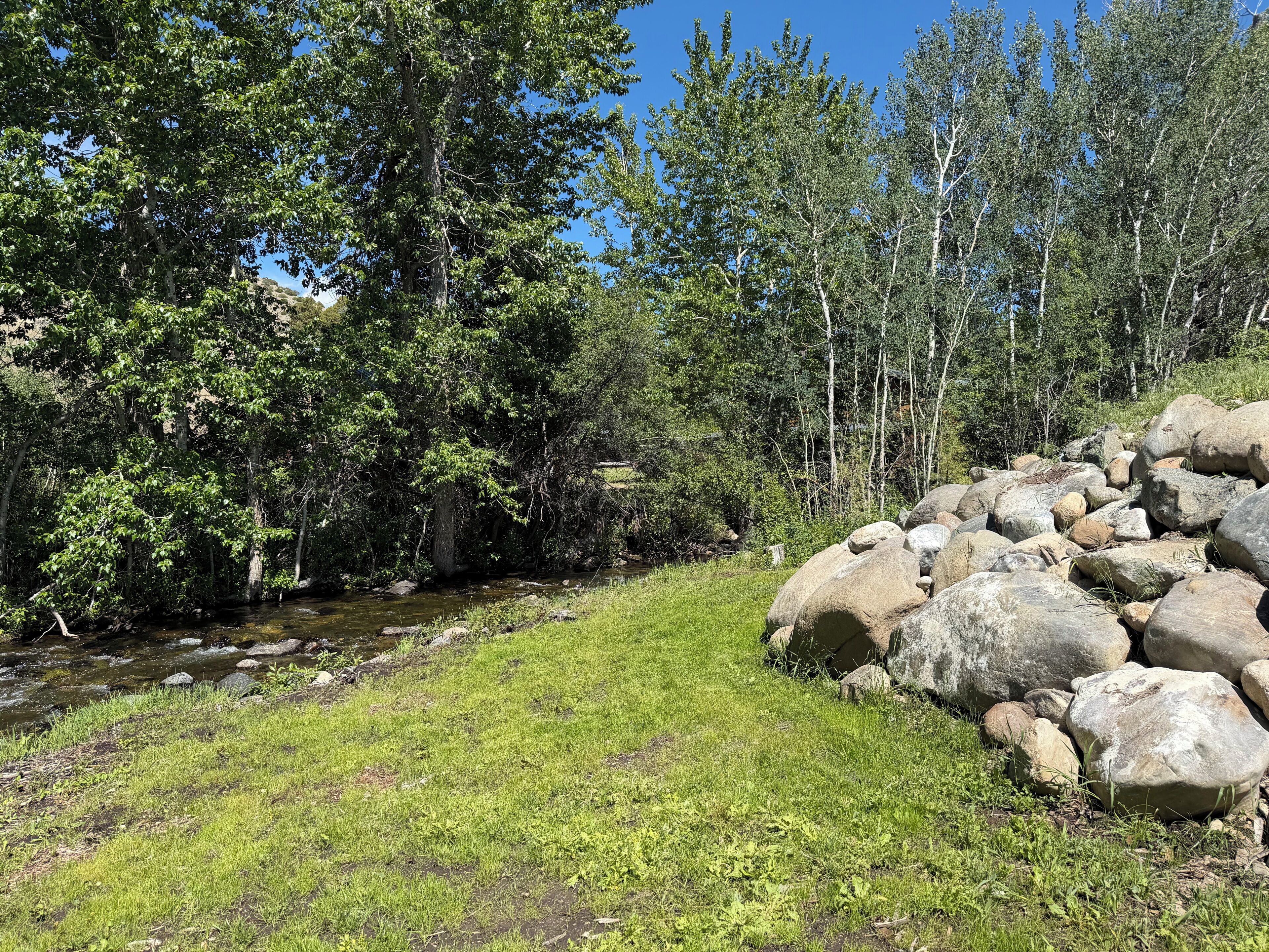 A natural landscape with a grassy area, a small stream, and a pile of rocks.