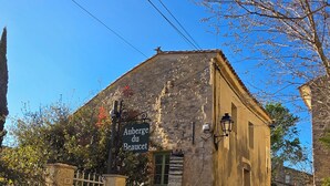 Ein Steinhaus mit einem Schild, auf dem 'Auberge du Beauquet' steht, einem verschlossenen Eingang und Kübelpflanzen.