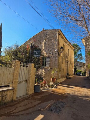 A stone building with a sign reading 'Auberge du Beauquet,' a gated entrance, and potted plants. - Le petit Beaucet: Elegance and gentle living in the heart of Provence (Le Beaucet)