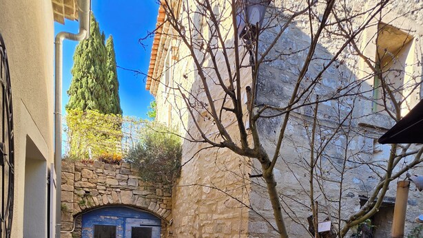 Ein schmaler Innenhof mit Steinmauern, ein kleiner Garten mit Topfpflanzen, eine blaue Tür und eine Steintreppe.