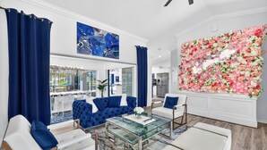 En moderne stue med et glas sofabord, hvide sofaer og et stort blomsterbillede.
