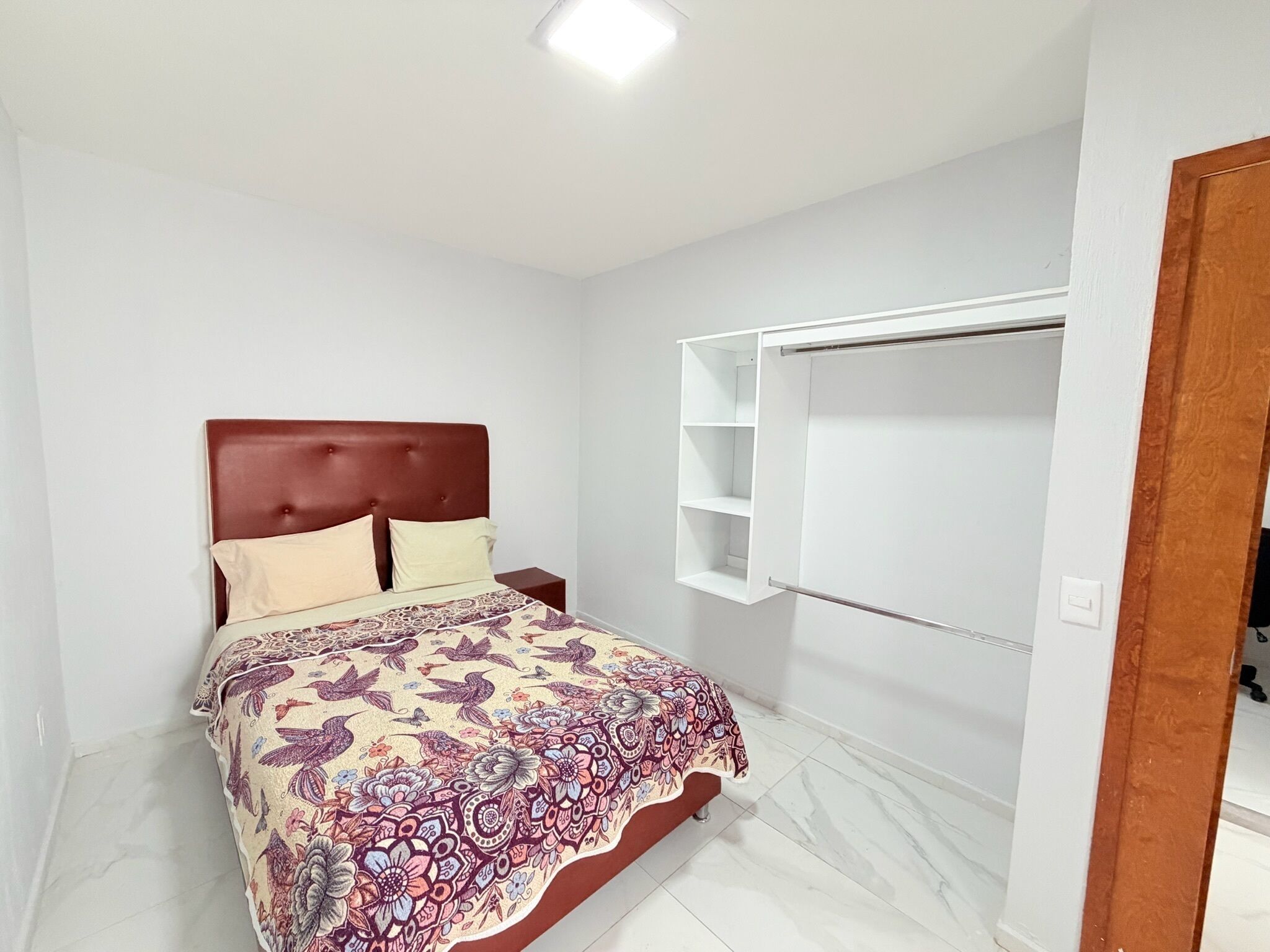 A bedroom with a bed, a nightstand, a wardrobe, and a ceiling light.