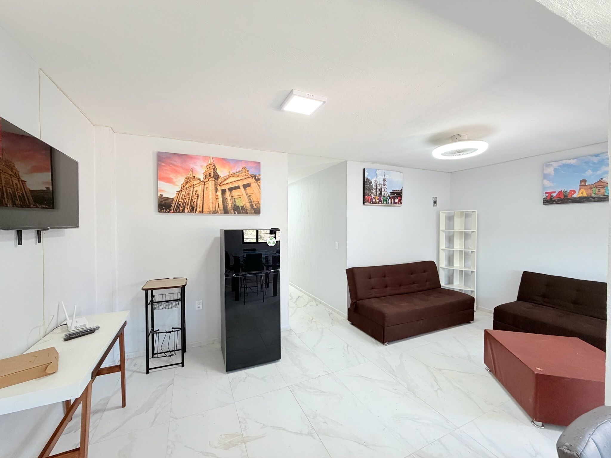 A modern living room with a sofa, a coffee table, a TV, and a refrigerator.