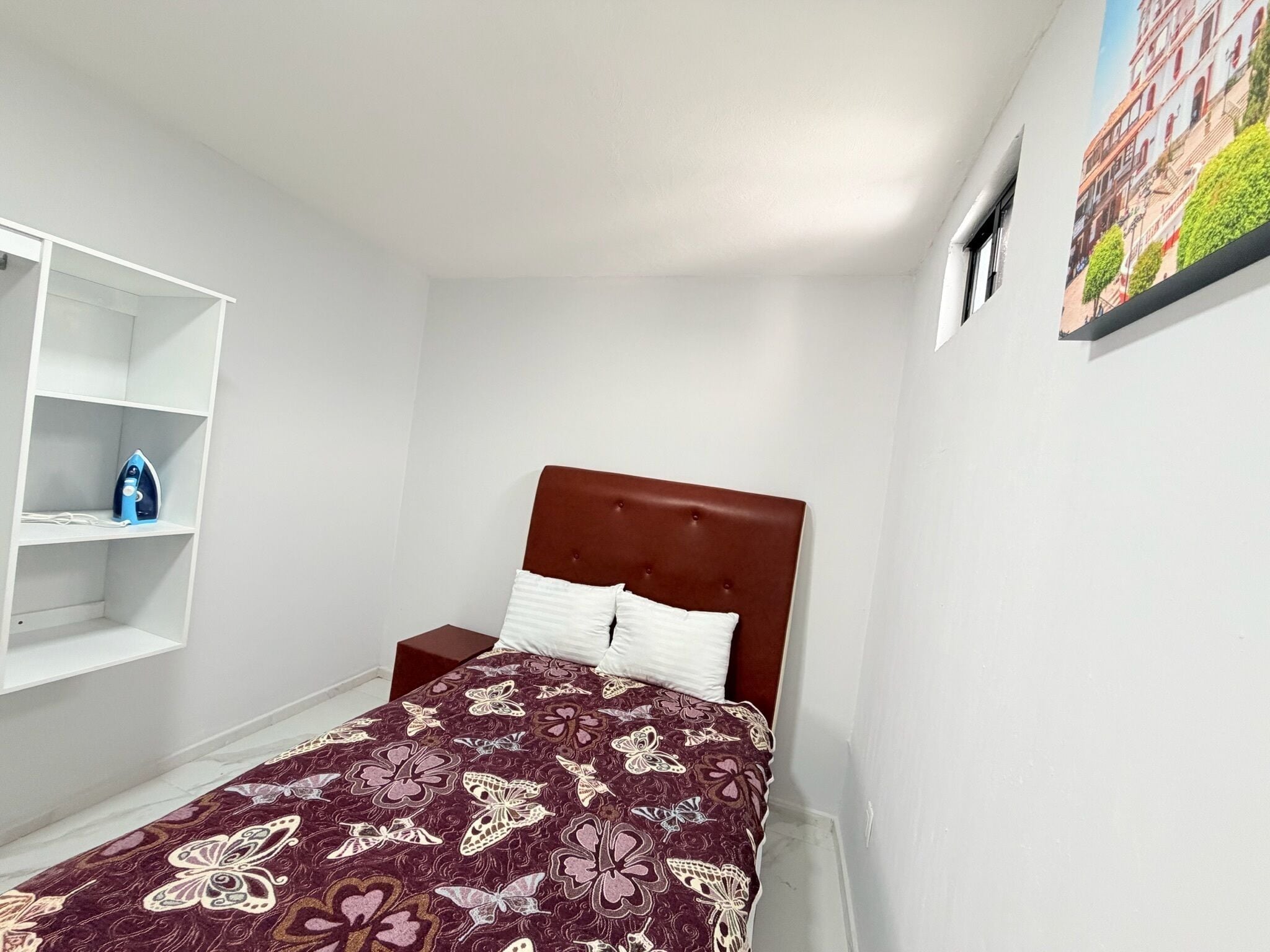 A bedroom with a bed, a nightstand, a wardrobe, and a painting on the wall.