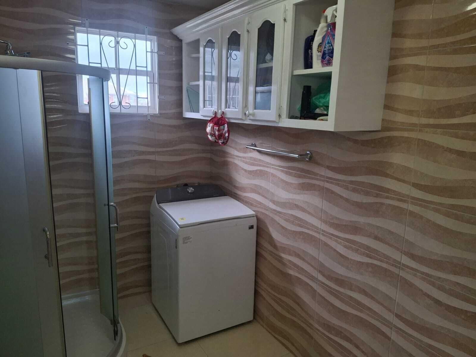 A compact bathroom with a washing machine, a glass door shower, and a cabinet with toiletries.