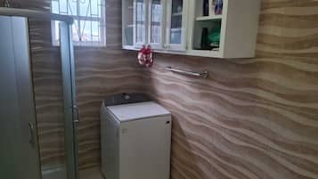 A compact bathroom with a washing machine, a glass door shower, and a cabinet with toiletries.