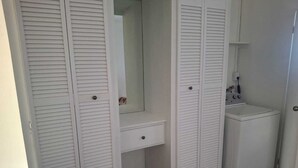 Een kamer met een ingebouwde wasmachine, een spiegel en een klein bankje.