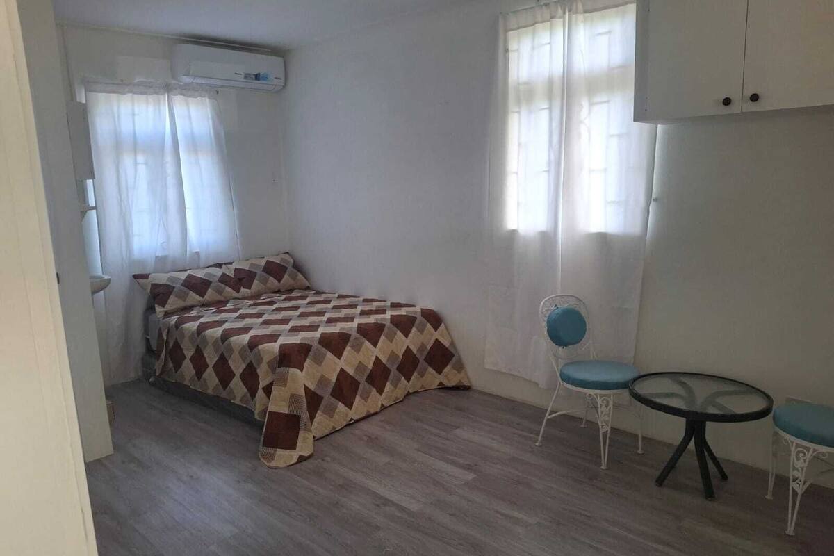 Un dormitorio con cama, una silla, una mesita y un equipo de aire acondicionado.