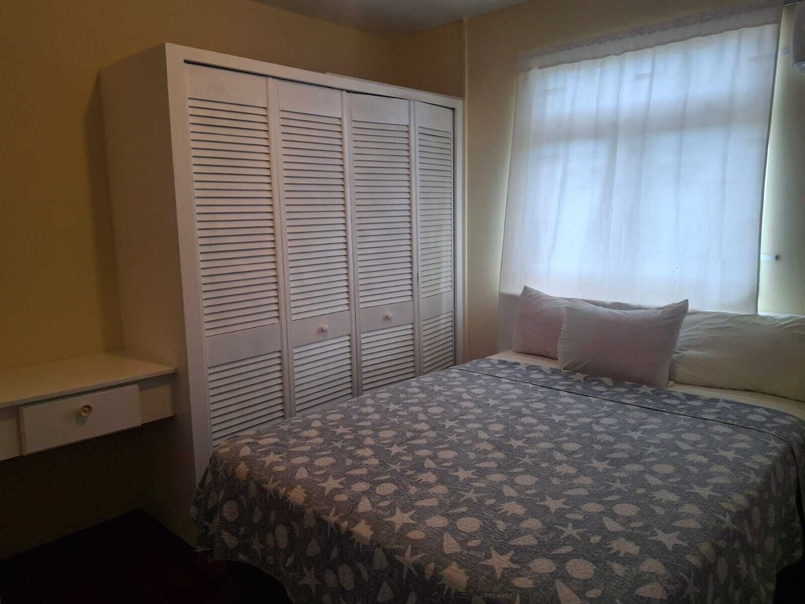 A bedroom with a bed, a wardrobe, a window with curtains, and a bedside table.