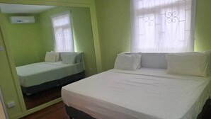 Een kamer met een groot bed, een kleiner bed, een raam met gordijnen en een luchtverkoeler aan de muur.