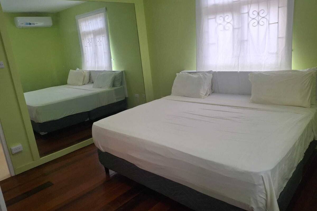 Una habitación con una cama grande, una cama más pequeña, una ventana con cortinas y un aire acondicionado instalado en la pared.