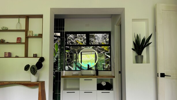 A bedroom with a bed, a bedside table, a mirror, a window with a view of greenery, and a door. - Stunning 2BR Home with Fast WiFi & AC – Mountain Views & Lush Nature, Ojochal (Puntarenas Province)