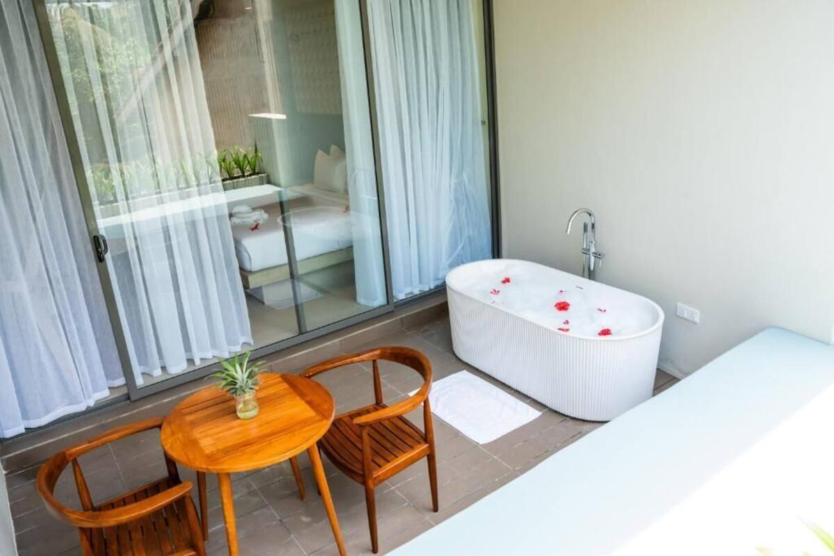 A modern bathroom with a freestanding bathtub, a wooden table with chairs, and a glass door leading to a balcony.