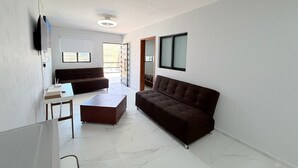 A spacious living room with a brown sofa, a coffee table, and a flat-screen TV mounted on the wall. - Residencia Gran Coyula Orange 510A (Tonala)